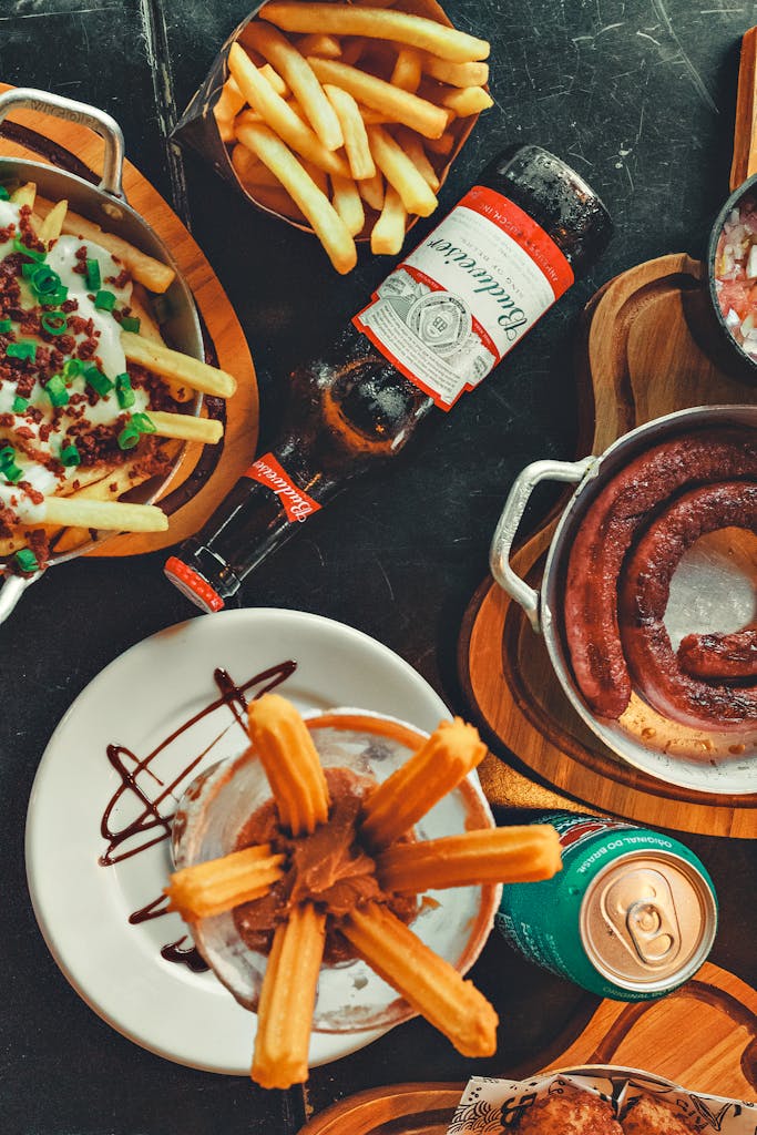 A delightful flat lay of various foods and beverages including churros and sausages.