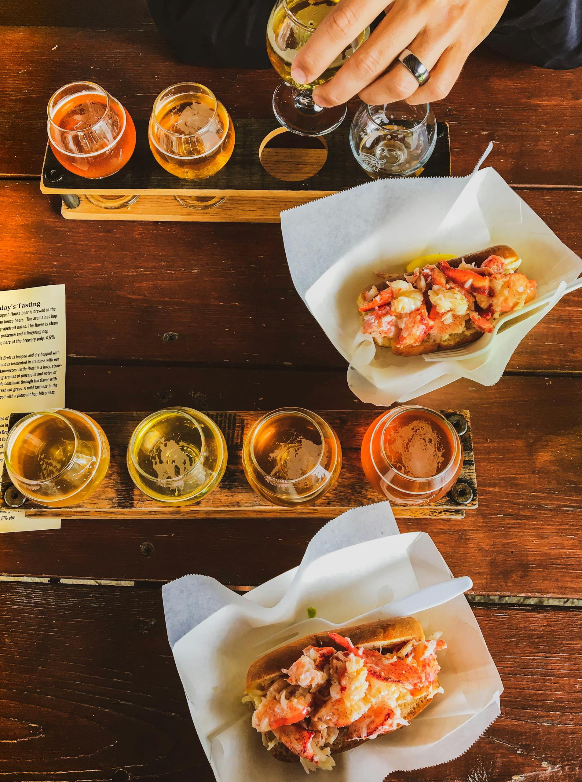 Top view of craft beer flight and lobster rolls on a rustic wooden table, offering a gourmet dining experience.