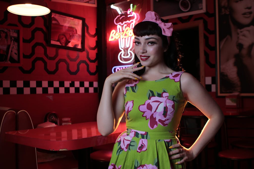 Woman in floral gown posing in vintage retro diner with nostalgic decor.