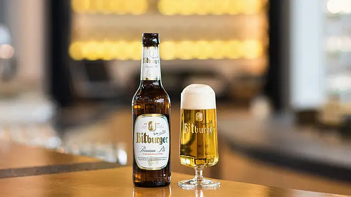 Botella y copa de Bitburger Premium Pils servida en barra con fondo de bar difuminado, estética cervecera alemana tradicional profesional