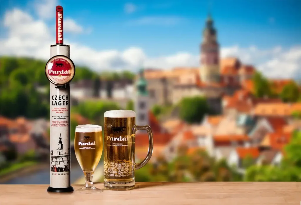 Grifo de cerveza Pardál Czech Lager con copa tulipa y jarra servidas, castillo Český Krumlov desenfocado al fondo, presentación comercial estética checa tradicional
