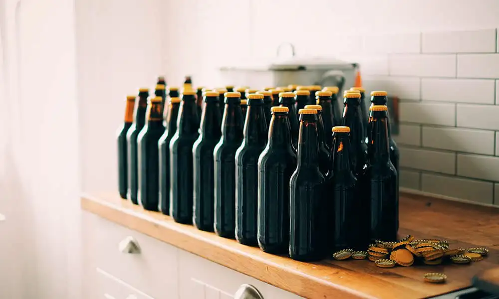 Botellas de cerveza casera usada para el envasado alineadas con tapones corona sobre una encimera de madera.
