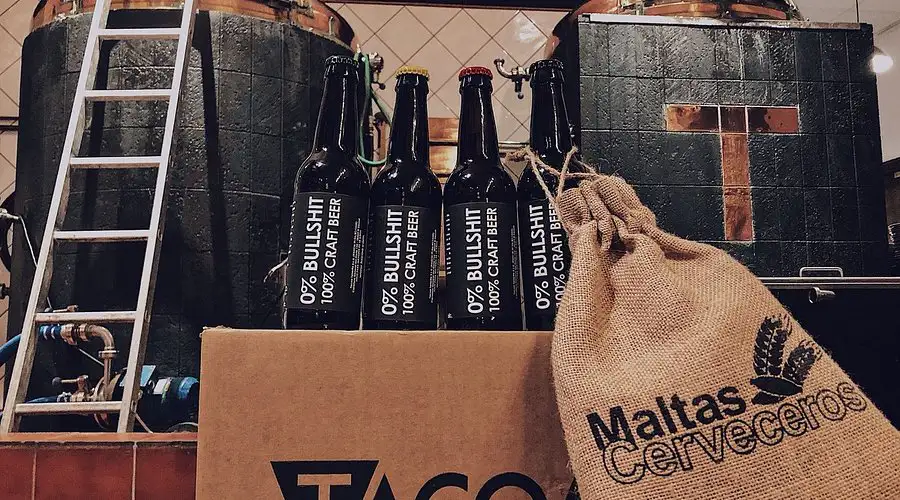 Interior de la microcervecería y brew‑restaurant Tacoa, con botellas y sacos de materias primas frente a los equipos de elaboración.