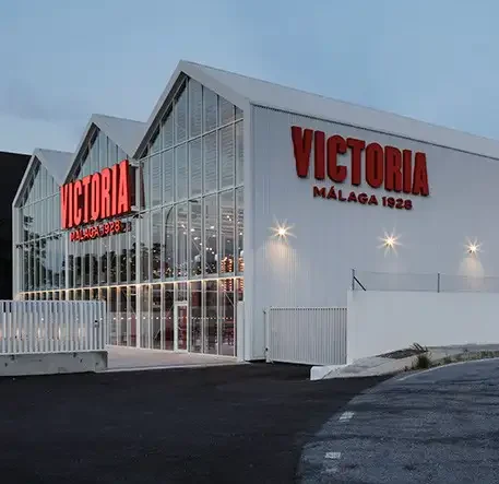 Fachada moderna de la nueva fábrica de Cerveza Victoria en Málaga con el letrero rojo "Victoria Málaga 1928".