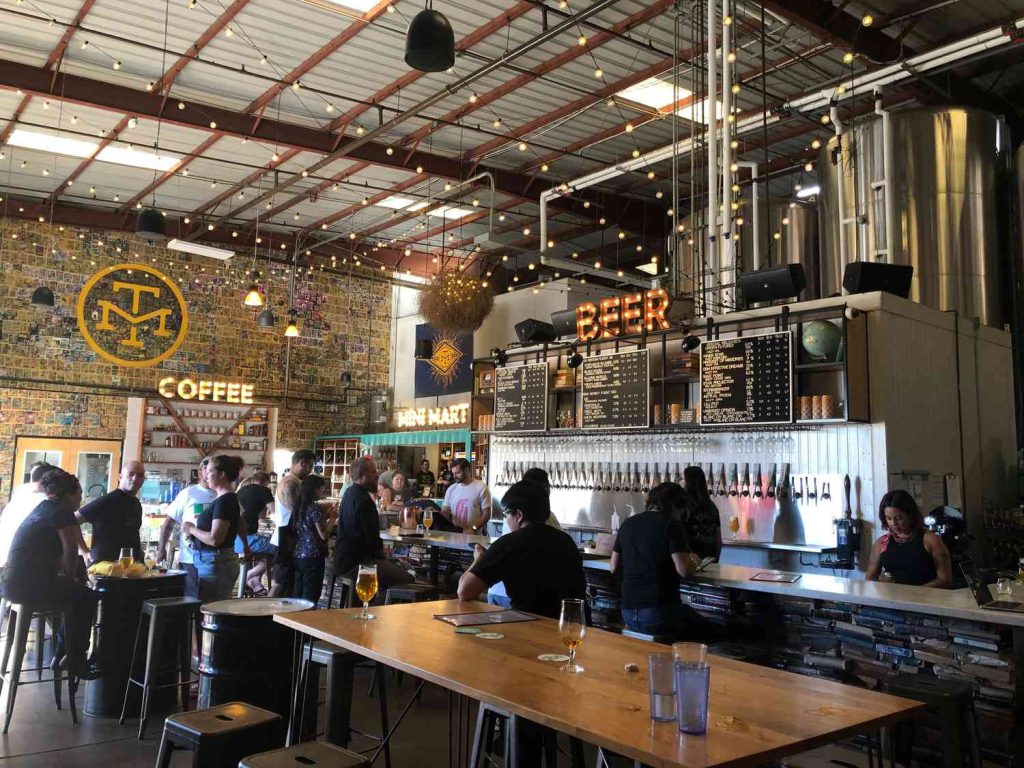 nterior del taproom de Modern Times Beer en Point Loma, San Diego - Tanques de fermentación, wall of cans y estética retrofuturista de la cervecera craft más innovadora de California
