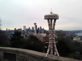 Seattle en una imagen: el skyline moderno dominado por el Space Needle convive con la torre de latas Rainier, recordatorio de que esta ciudad fue cervecera mucho antes del boom tech. Esas latas apiladas no son arte random - son homenaje a la 'R' roja que definió la identidad líquida de Seattle desde 1878. Mientras Amazon y Microsoft transformaron la ciudad, Rainier sigue siendo el denominador común entre el viejo Seattle de clase trabajadora y el nuevo Seattle de millonarios tech. Es la perfecta metáfora visual de Washington