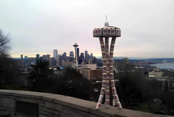 Seattle en una imagen: el skyline moderno dominado por el Space Needle convive con la torre de latas Rainier, recordatorio de que esta ciudad fue cervecera mucho antes del boom tech. Esas latas apiladas no son arte random - son homenaje a la 'R' roja que definió la identidad líquida de Seattle desde 1878. Mientras Amazon y Microsoft transformaron la ciudad, Rainier sigue siendo el denominador común entre el viejo Seattle de clase trabajadora y el nuevo Seattle de millonarios tech. Es la perfecta metáfora visual de Washington