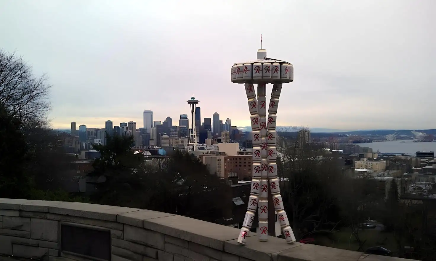 Seattle en una imagen: el skyline moderno dominado por el Space Needle convive con la torre de latas Rainier, recordatorio de que esta ciudad fue cervecera mucho antes del boom tech. Esas latas apiladas no son arte random - son homenaje a la 'R' roja que definió la identidad líquida de Seattle desde 1878. Mientras Amazon y Microsoft transformaron la ciudad, Rainier sigue siendo el denominador común entre el viejo Seattle de clase trabajadora y el nuevo Seattle de millonarios tech. Es la perfecta metáfora visual de Washington