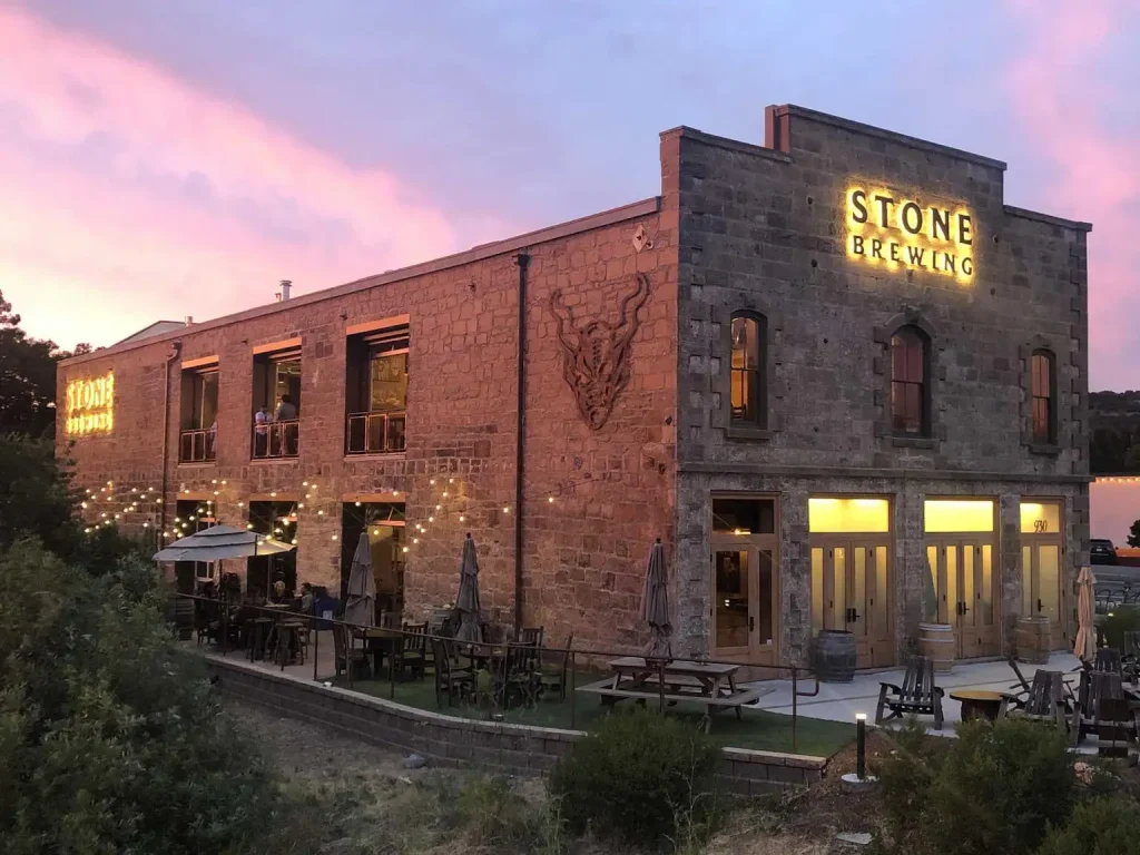 Fachada de piedra de Stone Brewing con su icónico logo de gárgola iluminado al atardecer en Escondido, California - Pioneros de la West Coast IPA extrema