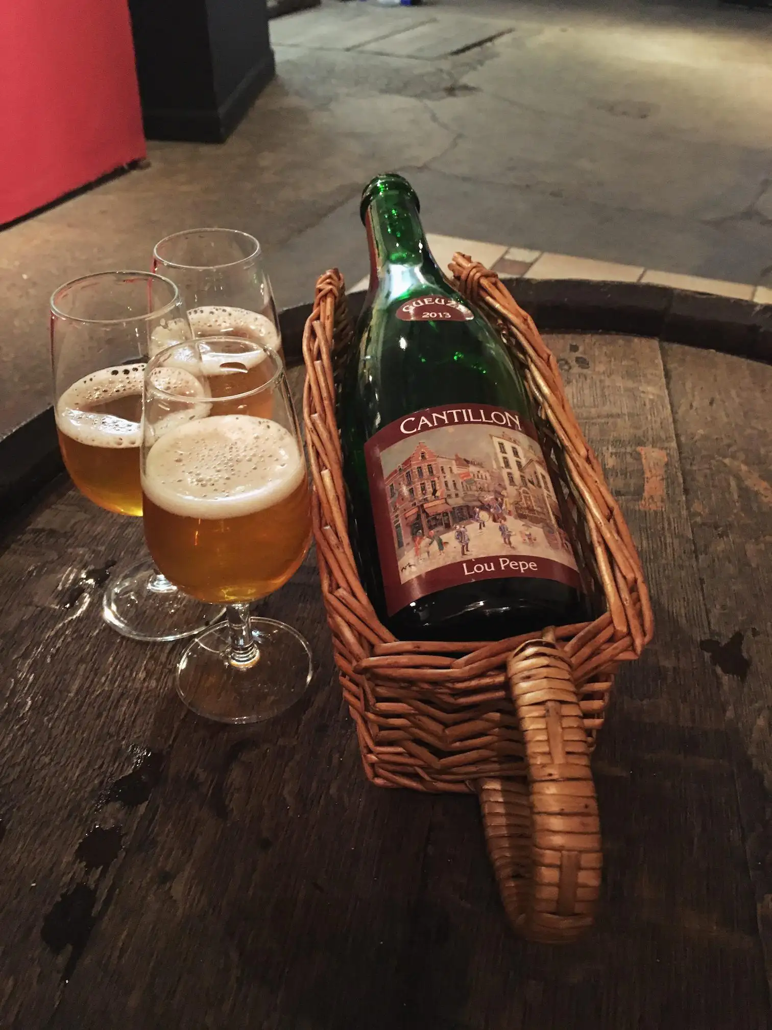 Cantillon Lou Pepe Kriek servida en copas con botella en cesta tradicional belga - Ejemplo de fermentación espontánea dentro de las llamadas cervezas sour